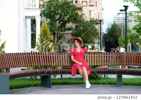 Woman in red dress and hat poses thoughtfully on park bench. Woman in red dress and hat poses thoughtfully on park bench. 127661452