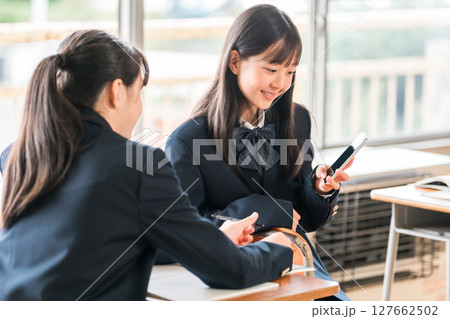 学校の教室でスマホを見ながら会話する中学生の女子生徒 127662502