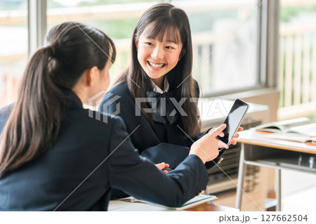 学校の教室でスマホを見ながら会話する中学生の女子生徒 127662504