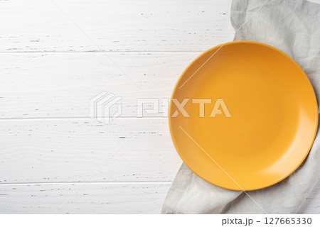 Yellow ceramic plate on a white wooden background. Top view. Yellow ceramic plate on a white wooden background. Top view. 127665330