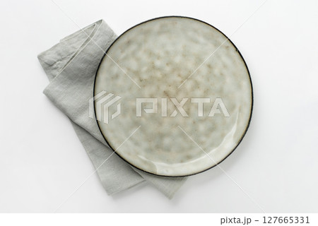 An empty grey textured plate with a napkin on a white table An empty grey textured plate with a napkin on a white table 127665331