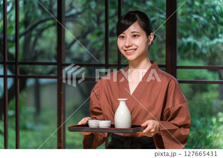 客室に日本酒を運ぶ仲居さん,旅館スタッフの女性 127665431