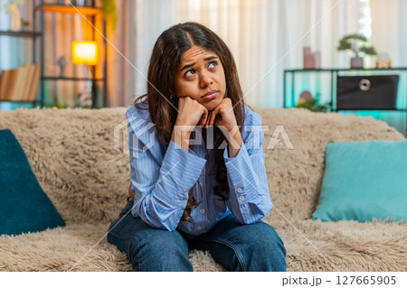 Indian woman feeling heartbroken after breakup with sad emotional face and low energy on home sofa 127665905
