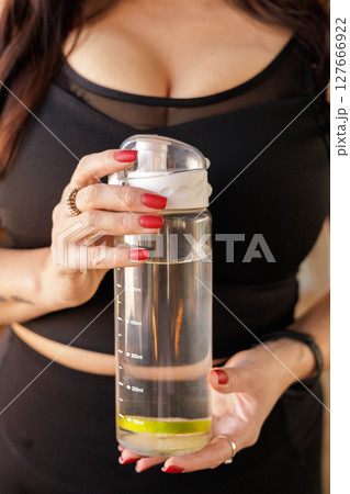 Close-up of plus-size woman holding water bottle with lemon slice after workout, body positive 127666922