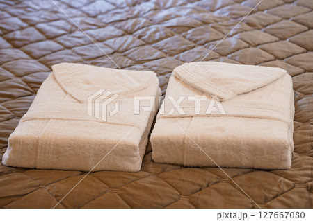 Plush Cream Bath Robes Folded on Quilted Bedspread, Luxury Spa Hotel Comfort, Soft Texture and Relaxing Atmosphere, Beige and Brown Tones 127667080