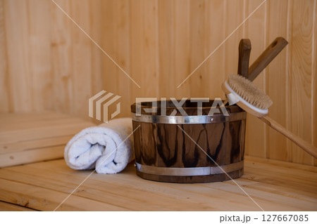 Traditional Wooden Sauna Interior with Bucket, Brush, and Towel: Rustic Relaxation Scene Featuring Natural Light and Warm Wood Tones 127667085