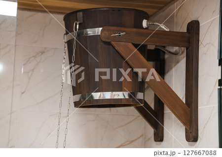 Rustic Wooden Bucket Hanging in Sauna with Steel Band and Mount Against Tiled Wall. Dark Brown, Relaxing Spa Theme. 127667088