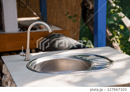 Outdoor Kitchen Sink with Modern Faucet, Rustic Counter, Wood Cabinet and Blue Accents: Bright Summertime Scene Outdoor Kitchen Sink with Modern Faucet, Rustic Counter, Wood Cabinet and Blue Accents: Bright Summertime Scene 127667103