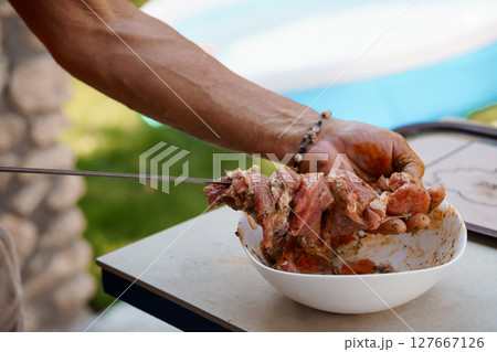 Culinary Preparation of Marinated Meat Outdoors: Chef Carving Ribs with Knife in Bowl on Table with Blurred Scenic Seaside Backdrop 127667126