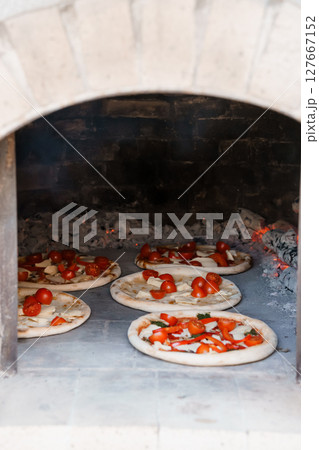 Rustic Wood-Fired Oven Baking Classic Margherita Pizzas: Close-Up of Fresh Tomatoes, White Dough, Brick Interior, and Warm Lighting Rustic Wood-Fired Oven Baking Classic Margherita Pizzas: Close-Up of Fresh Tomatoes, White Dough, Brick Interior, and Warm Lighting 127667152