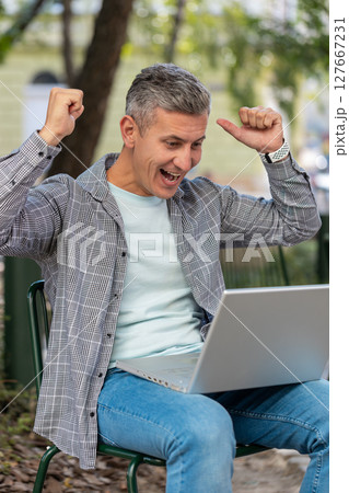 Happy man freelancer working on laptop screams in triumph win celebrating success sitting on chair Happy man freelancer working on laptop screams in triumph win celebrating success sitting on chair 127667231