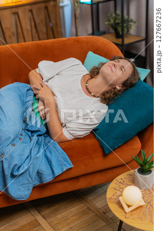 Sick ill young woman lady suffering from period cramps, painful stomach ache on sofa couch at home 127667236