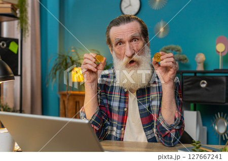 Senior old grandfather man freelancer holding two gold BTC coins successful developer programmer 127667241