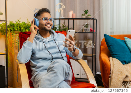 Happy relaxed man in wireless headphones dancing listening favorite disco pop music on home chair Happy relaxed man in wireless headphones dancing listening favorite disco pop music on home chair 127667346