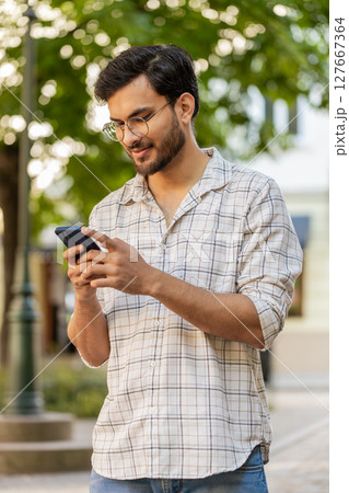 Indian young man using smartphone typing text messages in social media application online on street Indian young man using smartphone typing text messages in social media application online on street 127667364