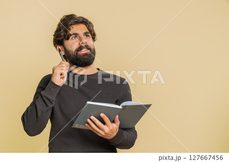 Thoughtful businessman making notes, writing down thoughts with pen into diary on beige background Thoughtful businessman making notes, writing down thoughts with pen into diary on beige background 127667456