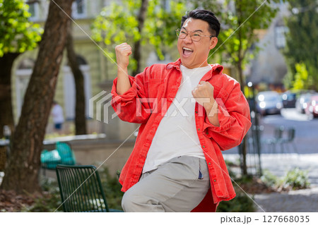 Asian man shouting celebrating success winning goal achievement good victory news on city street Asian man shouting celebrating success winning goal achievement good victory news on city street 127668035