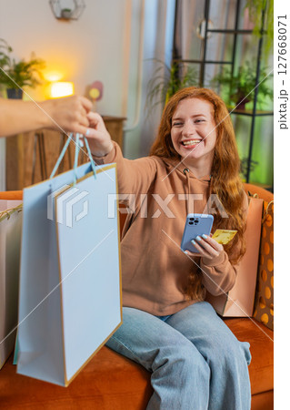Excited young Caucasian woman with shopping bags receiving order sitting on sofa couch at home 127668071