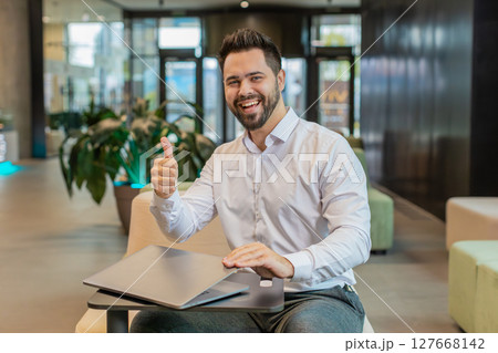 Smiling businessman closing laptop PC computer after finishing work sitting in modern office lobby 127668142