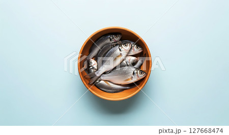 Six silver fish are neatly arranged in a wooden bowl. Their scales glisten under light, showcasing fresh details. The bowl is round, highlighting the fish's streamlined bodies 127668474