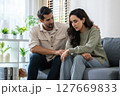 Supportive couple in emotional moment at home as woman struggles with sadness and stress, expressing 127669833