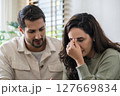 Supportive couple in emotional moment at home as woman struggles with sadness and stress, expressing 127669834