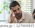 Supportive couple in emotional moment at home as woman struggles with sadness and stress, expressing 127669835