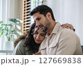 Supportive couple in emotional moment at home as woman struggles with sadness and stress, expressing 127669838