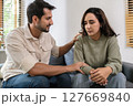 Supportive couple in emotional moment at home as woman struggles with sadness and stress, expressing 127669840