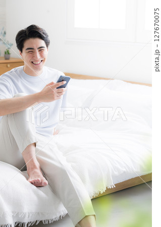 ベットでくつろぐスマホを持つ考える爽やかな男性の全身縦 127670075