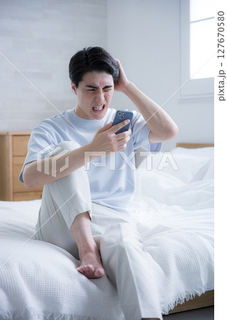 寝起きに不穏なメールやチャットを見てしまう若い男性　仕事困る 127670580