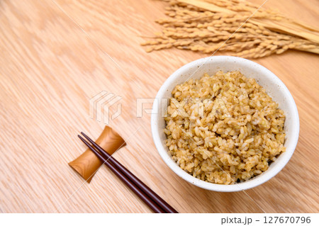 木目テーブル背景の茶碗に玄米ごはんと稲穂 127670796