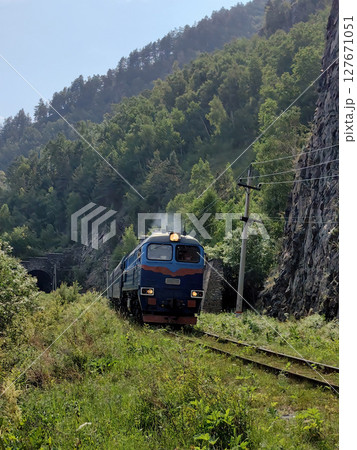 colorful train navigates through lush landscape near mountains during clear daytime. colorful train navigates through lush landscape near mountains during clear daytime. 127671051