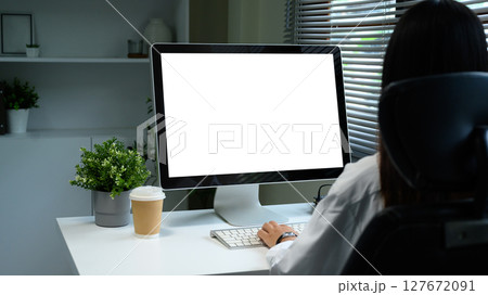 Back view of woman working at desktop computer with blank screen in a modern office Back view of woman working at desktop computer with blank screen in a modern office 127672091