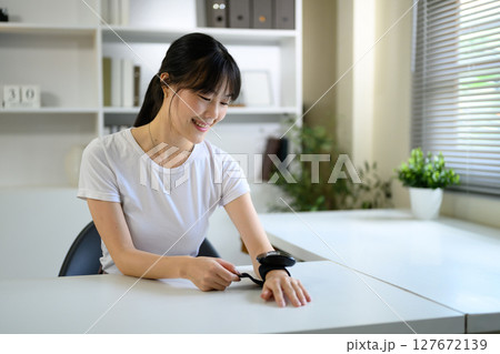 Asian woman checking pulse or blood pressure with smart wearable medical device. 127672139