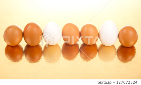 White and brown eggs lined up on a shiny golden background 127672324
