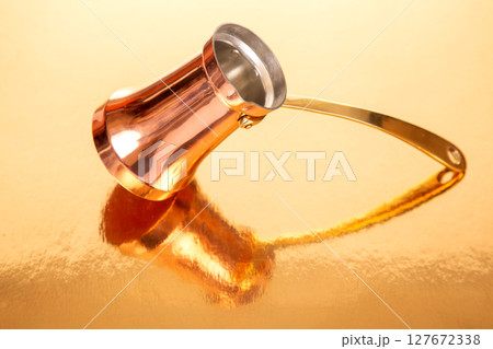copper Turkish coffee maker with a long brass handle, set against a minimalist golden background copper Turkish coffee maker with a long brass handle, set against a minimalist golden background 127672338