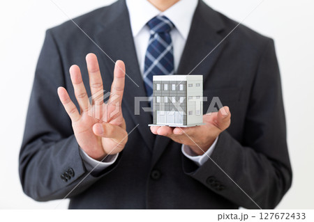 ビルの模型を持って4本指を立てるスーツ姿のミドル男性ビジネスマン 127672433