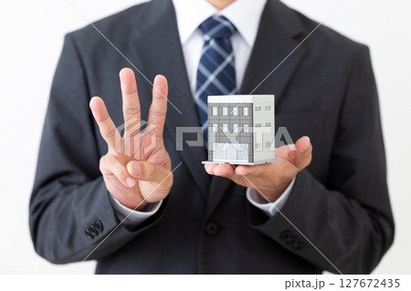 ビルの模型を持って3本指を立てるスーツ姿のミドル男性ビジネスマン 127672435