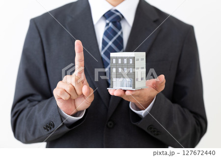 ビルの模型を持って人差し指を立てるスーツ姿のミドル男性ビジネスマン 127672440