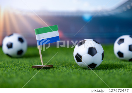 Small Sierra Leone flag with soccer balls on green grass, depicting national team pride for an international stadium football match 127672477