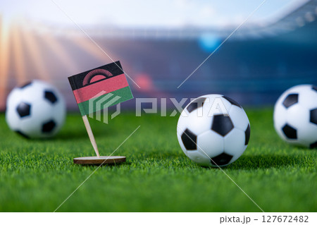 Malawian flag proudly stands with miniature soccer balls on green turf, symbolizing national football team spirit and global sports competition 127672482