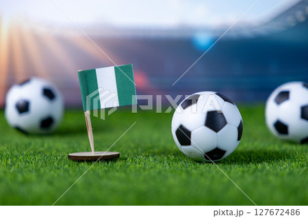 Nigerian flag with small soccer balls on a vibrant green football field representing international sports and national team championship tournaments 127672486