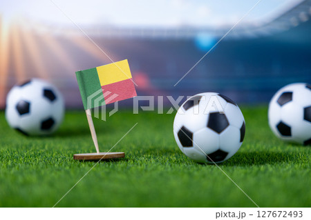 Benin national flag stands proudly on green artificial grass with mini soccer balls, symbolizing sports competition and patriotism in a stadium setting with copy space Benin national flag stands proudly on green artificial grass with mini soccer balls, symbolizing sports competition and patriotism in a stadium setting with copy space 127672493