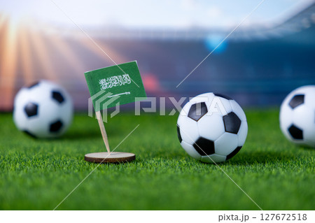 Miniature Saudi Arabian flag stands proudly on a green sports field with soccer balls, symbolizing national football pride and global championship aspirations 127672518