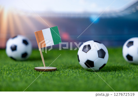 Ivory Coast national flag prominently displayed alongside miniature soccer balls on green grass, symbolizing international football competition and national pride 127672519