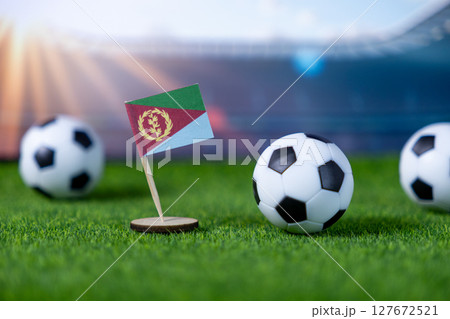 Miniature Eritrean flag stands proudly with soccer balls on vibrant green turf, symbolizing national team spirit in a global football stadium Miniature Eritrean flag stands proudly with soccer balls on vibrant green turf, symbolizing national team spirit in a global football stadium 127672521
