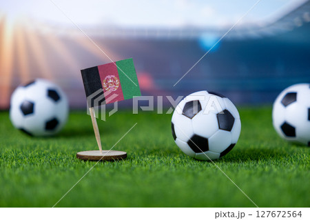 Afghanistan flag proudly on green artificial grass with soccer balls, representing national teams, international sports, and passionate global competition 127672564