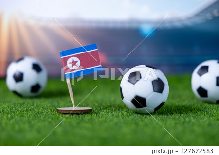 Miniature North Korean flag and small soccer balls on vibrant green grass, symbolizing global football tournaments and national sports representation within a stadium 127672583