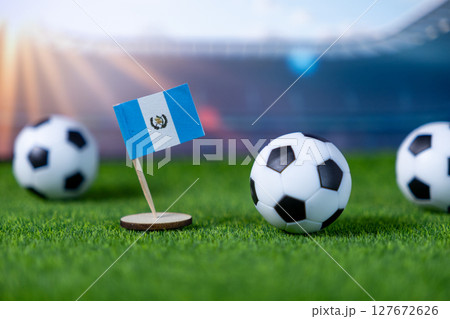 A small flag of Guatemala stands proudly on vibrant green grass with miniature soccer balls, symbolizing national pride and the excitement of international football competition A small flag of Guatemala stands proudly on vibrant green grass with miniature soccer balls, symbolizing national pride and the excitement of international football competition 127672626